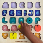 Colorful letter-shaped letters with symbols and a hand pointing to one of them on wood board.